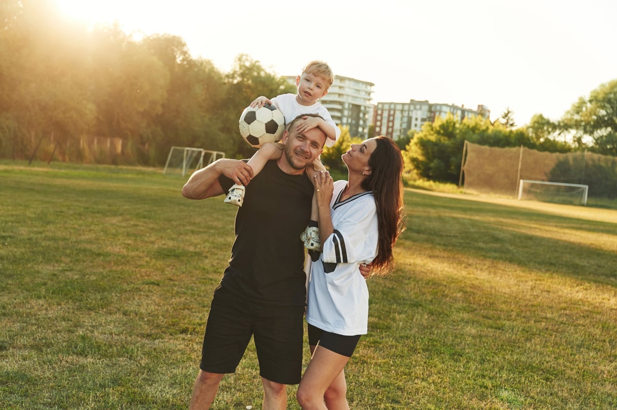 Family of father, mother and young son on the field with soccer ball.